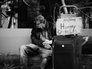 Homeless man with suitcase and sign asking for food