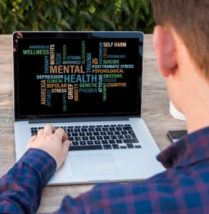 Teenage boy looking at mental health word cloud on a laptop computer