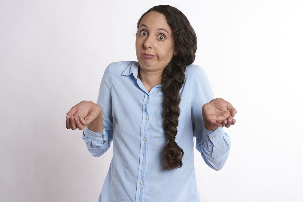 Confused woman shrugging her shoulders and gesturing with her hands as if asking "What?"