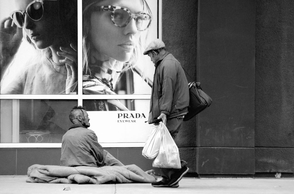 Rough sleeper talking to a shopper outside a Prada shop