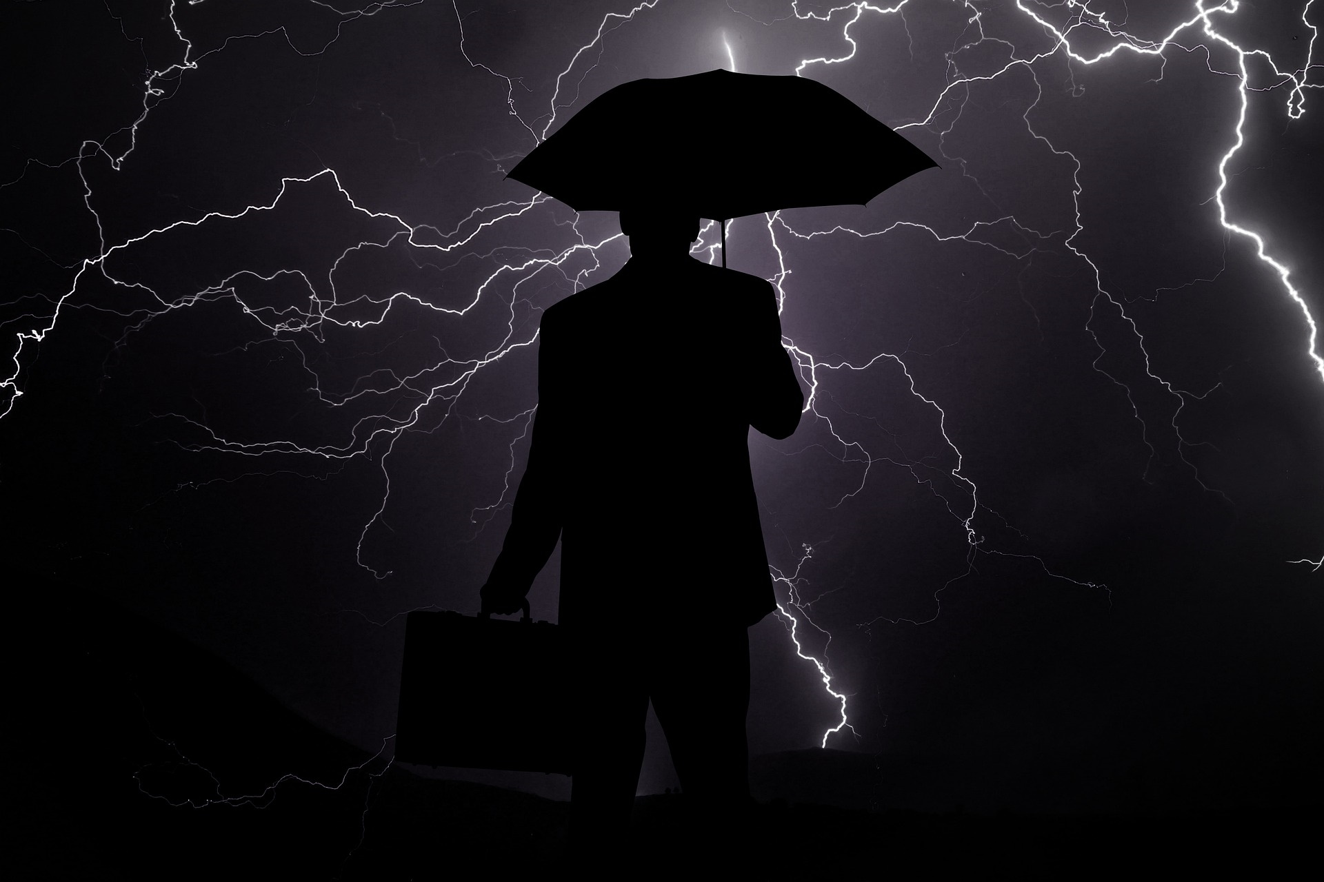 Silhouette of a businessman outside in a thunderstorm holding an umbrella and brielfase with lightning flashing behind him
