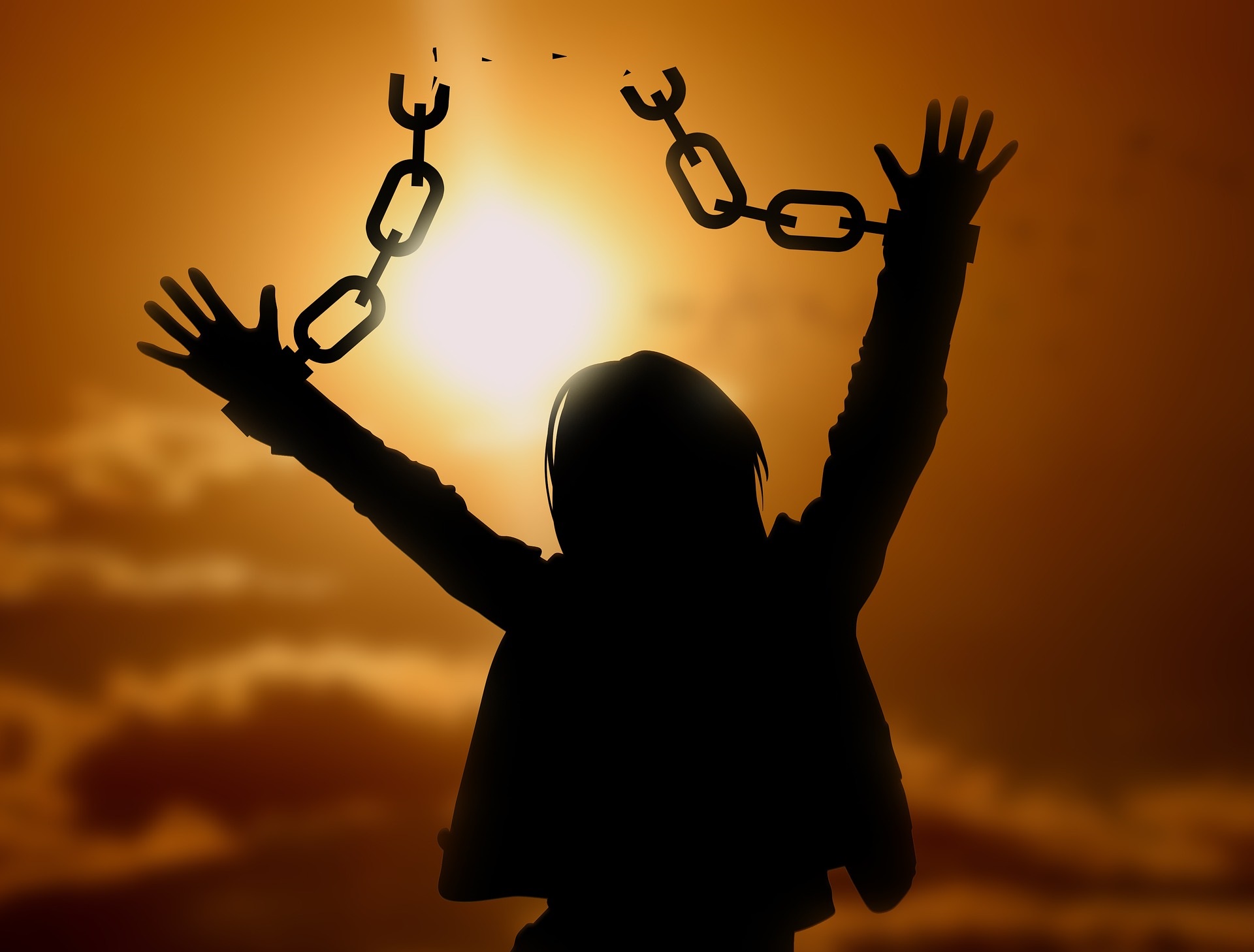 Silhouette of a woman breaking a chain to free her hands as the sun rises