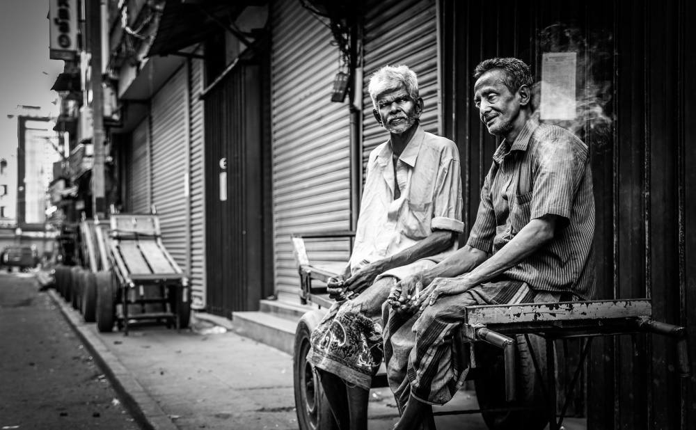 Two poor men sitting on a trolley on a street of closed shops. Petta, Colombo, Sri Lanka